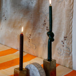 Two gold metal cubes candle holders with two candles on top, with a half-circled clay piece in the middle