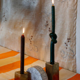 Two gold metal cubes candle holders with two candles on top, with a half-circled clay piece in the middle