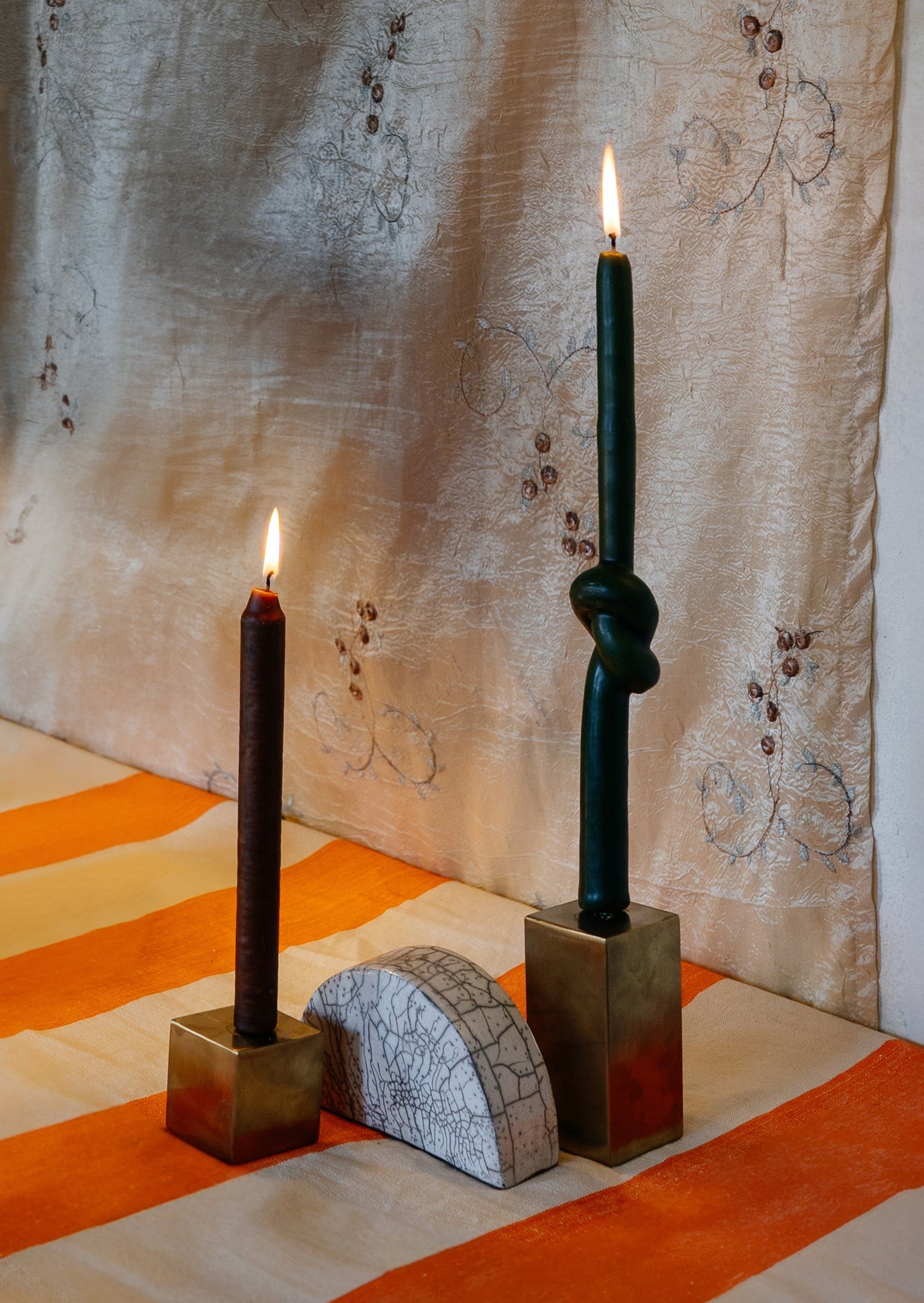 Two gold metal cubes candle holders with two candles on top, with a half-circled clay piece in the middle