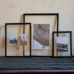 Three black wooden photo frames with transparent, double-layered glass in various sizes are resting on a wall.