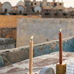 Two gold metal cube candle holders with candles on top, alongside a half-circled clay piece, featured in a photoshoot on a rooftop in Egypt.