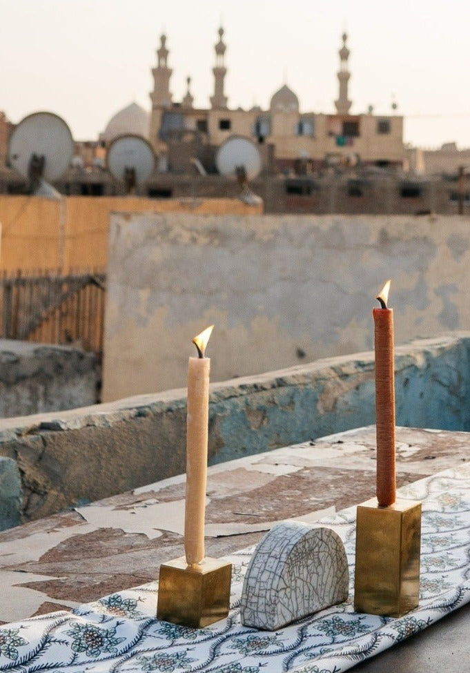 Two gold metal cube candle holders with candles on top, alongside a half-circled clay piece, featured in a photoshoot on a rooftop in Egypt.