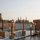 Two gold metal cube candle holders with candles on top, alongside a half-circled clay piece, featured in a photoshoot on a rooftop in Egypt.