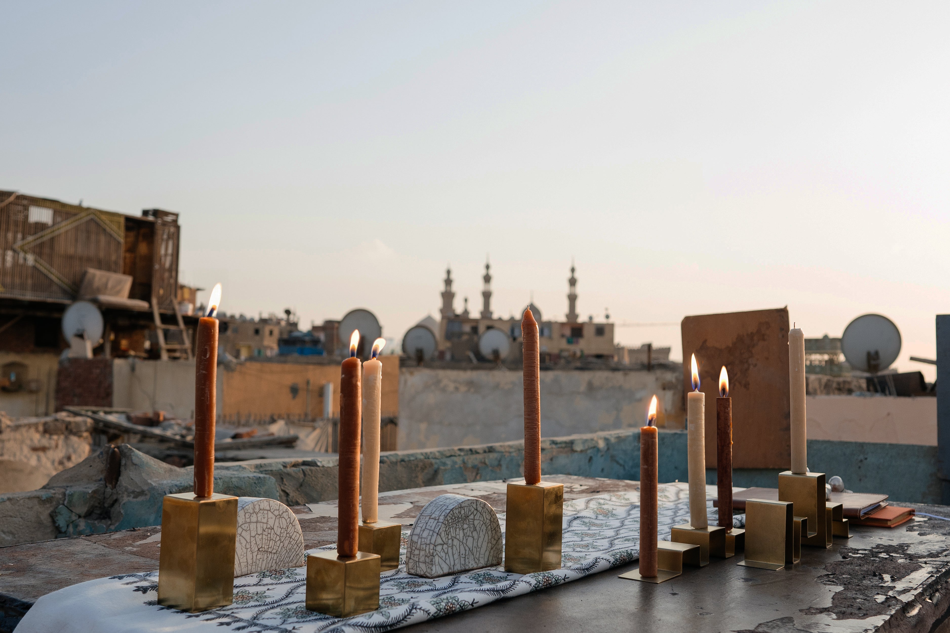 Two gold metal cube candle holders with candles on top, alongside a half-circled clay piece, featured in a photoshoot on a rooftop in Egypt.