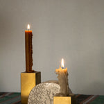 Two gold metal cubes candle holders with two candles on top, with a half-circled clay piece in the middle