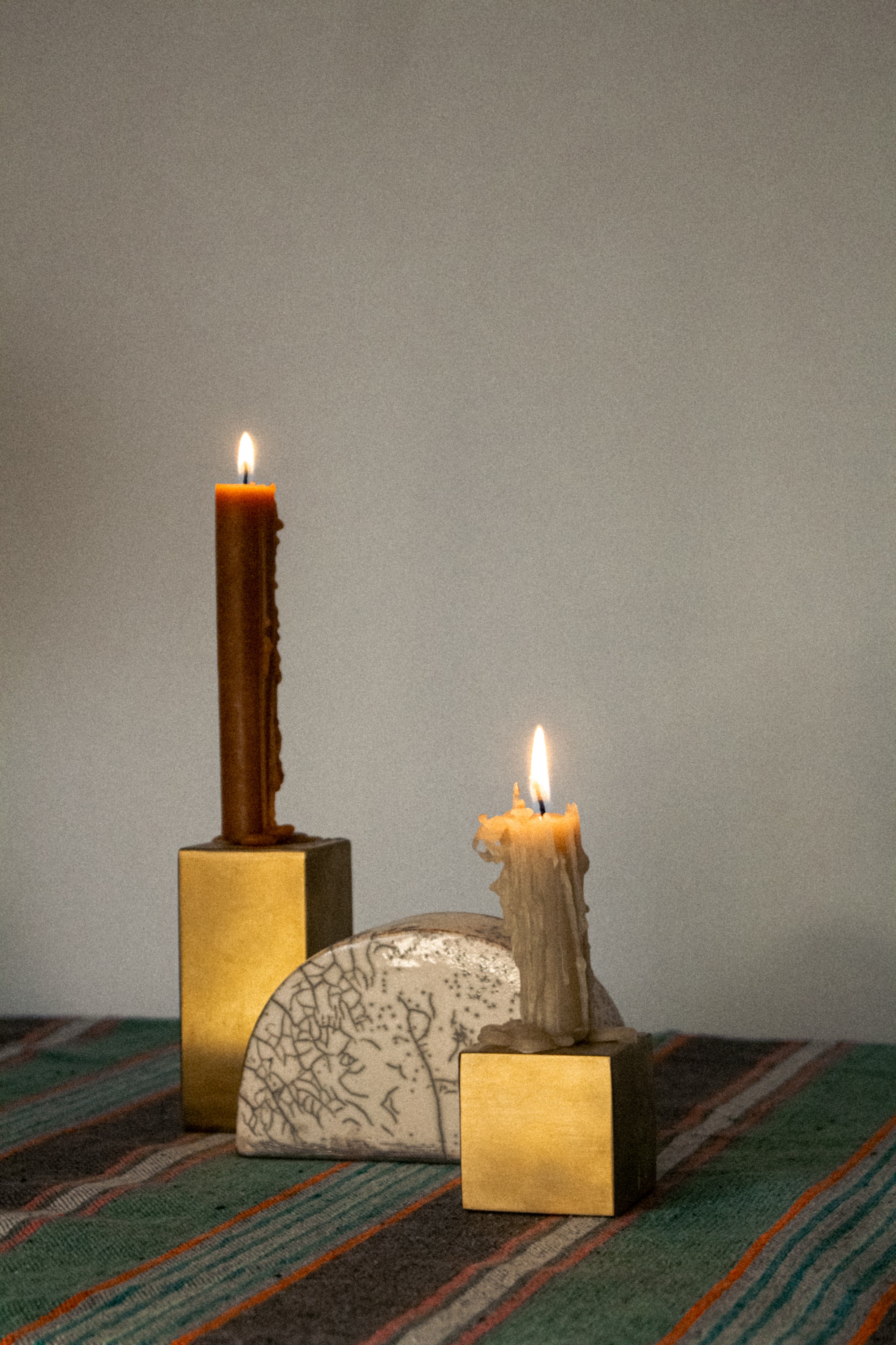 Two gold metal cubes candle holders with two candles on top, with a half-circled clay piece in the middle