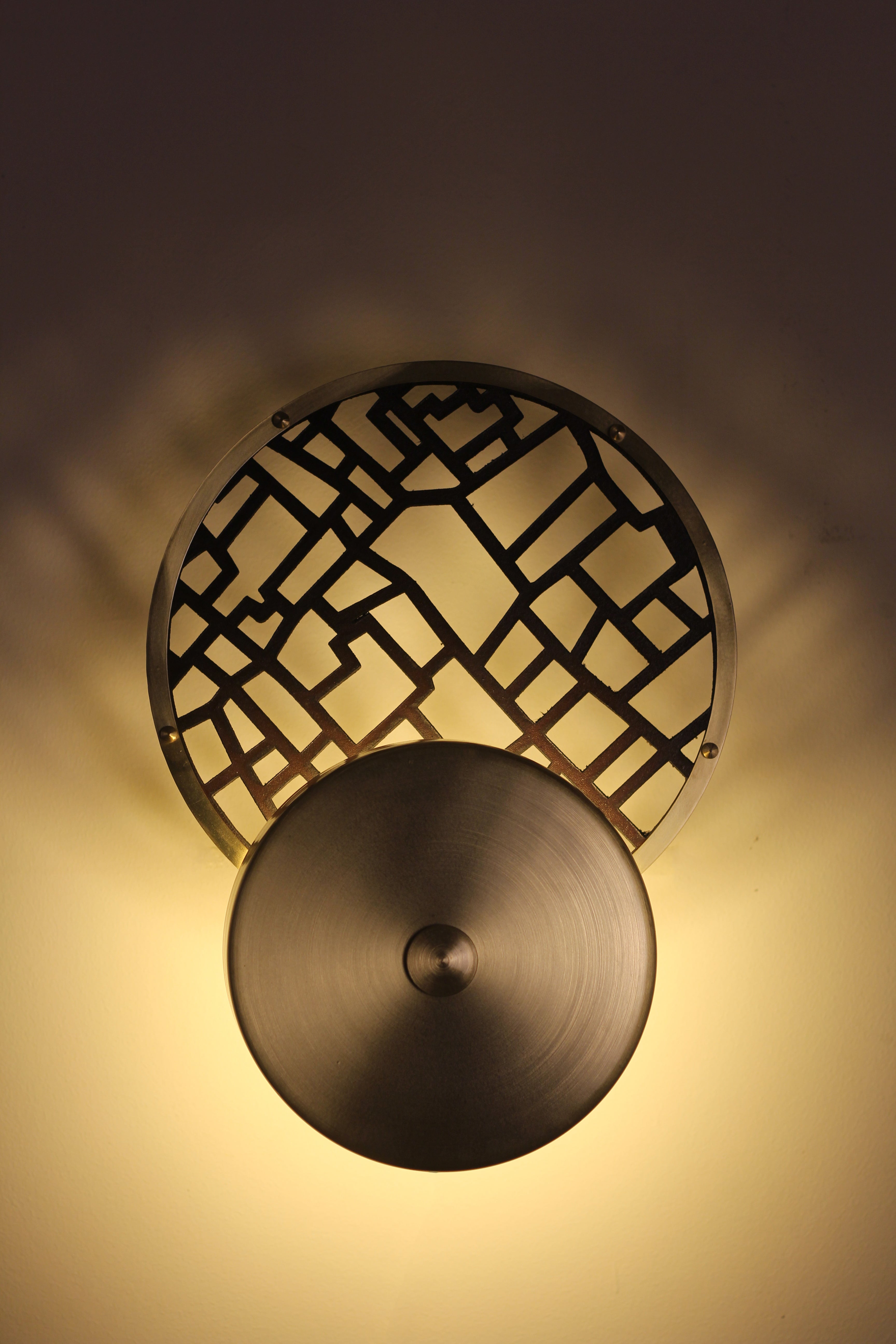 Double circle applique made of brass and grid-patterned leather, hung on a wall.