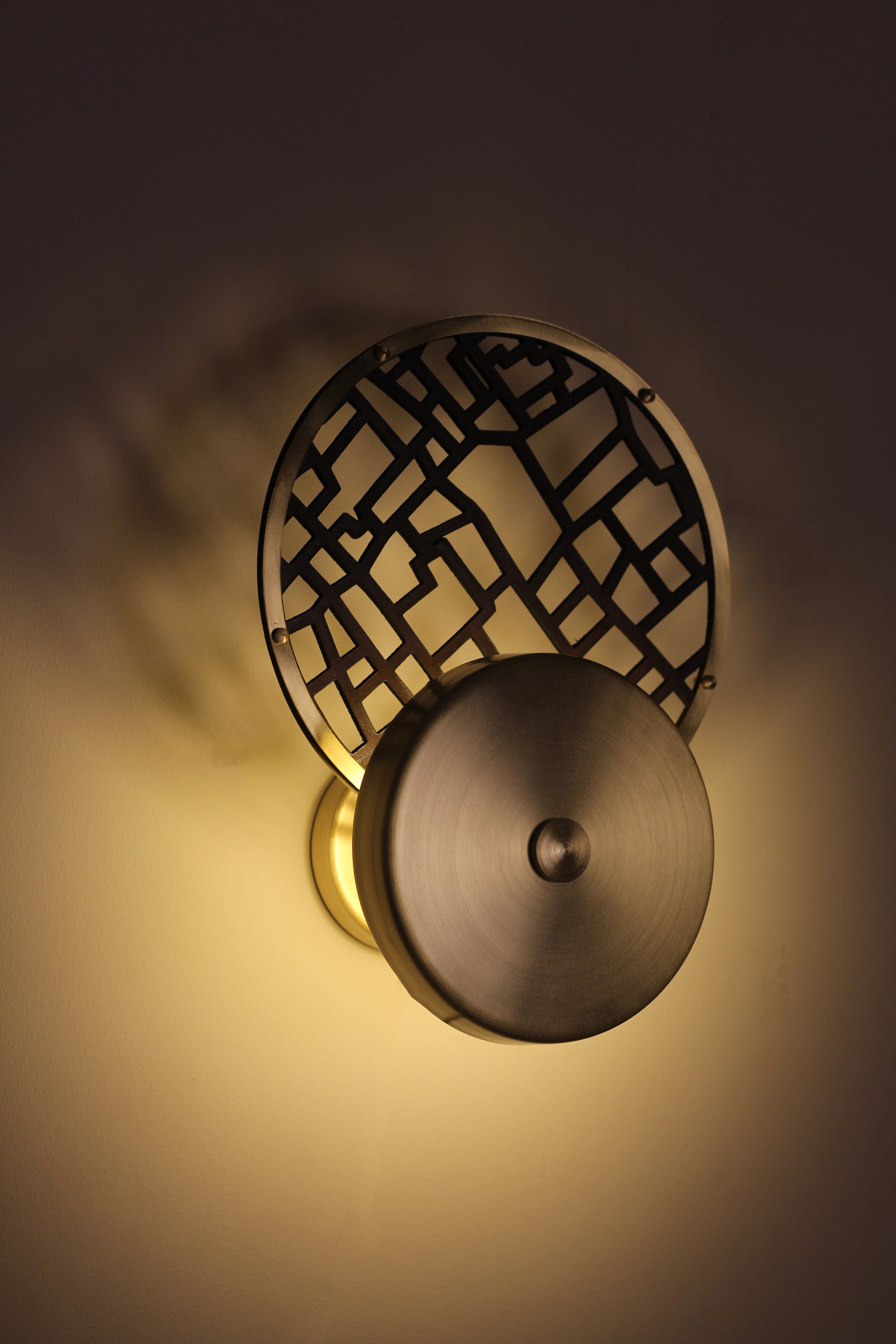 Double circle applique made of brass and grid-patterned leather, hung on a wall.