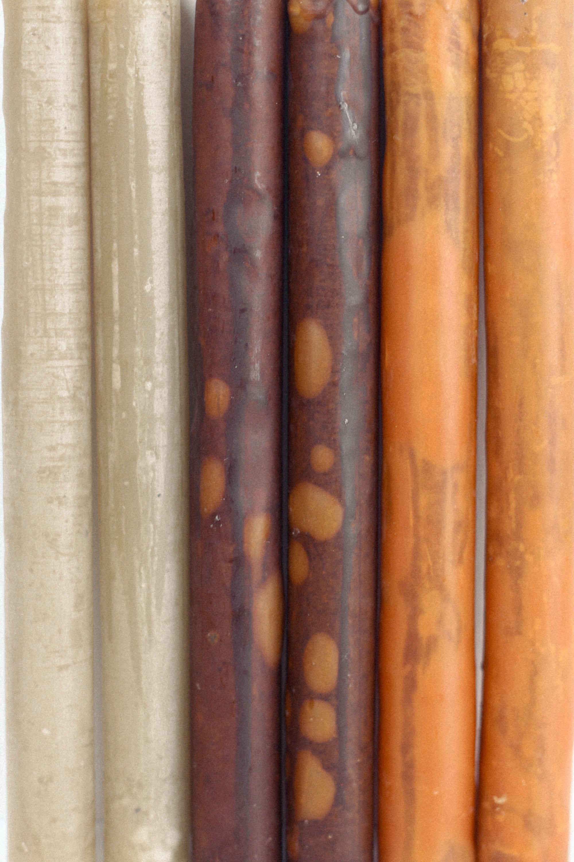 Close-up of six textured taper candles in brick, dust, and cotton colors.