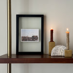 A small black wooden photo frame is placed on a shelf