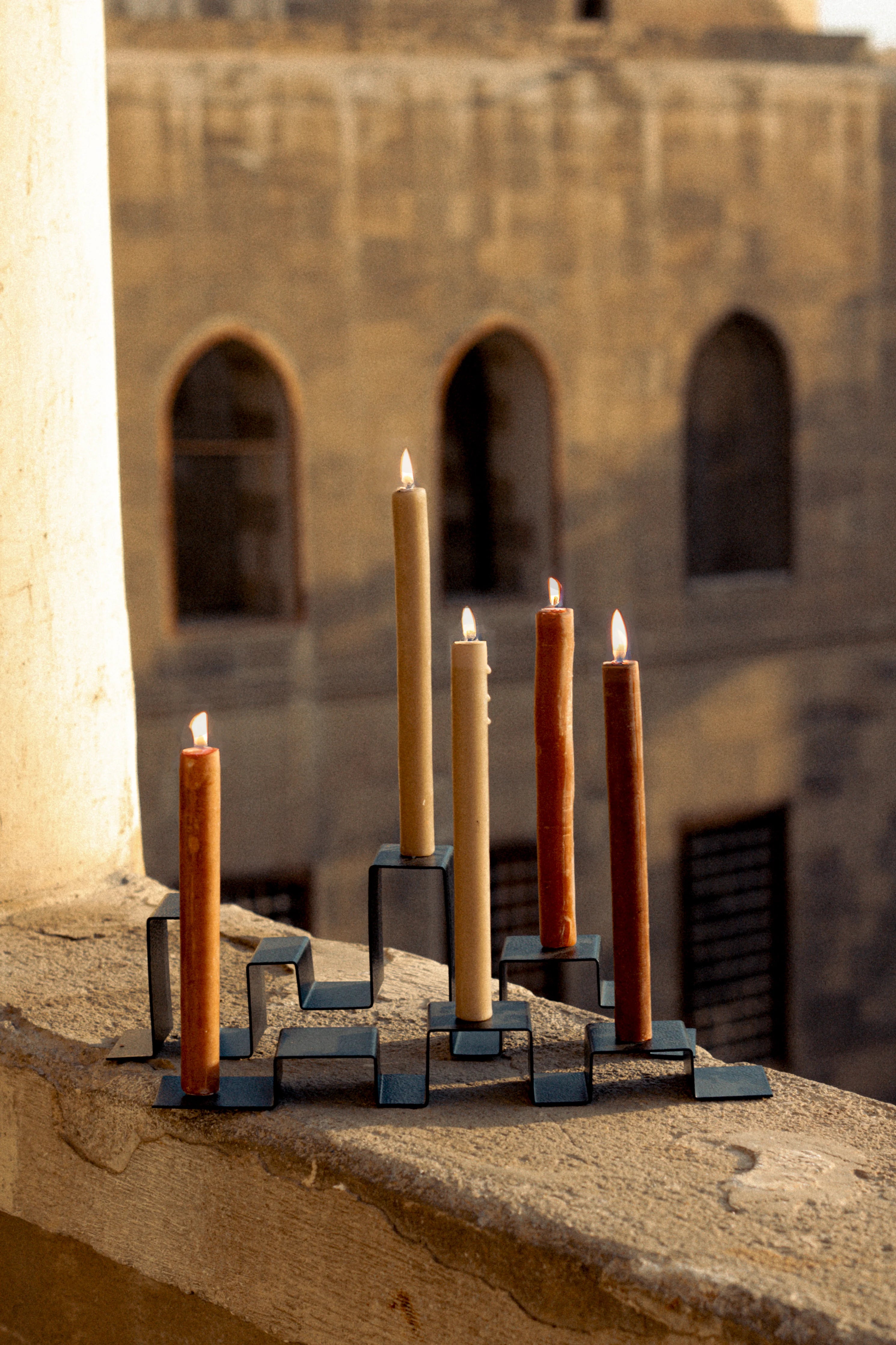 Two stainless steel candleholders holding a total of five candles set on a balcony